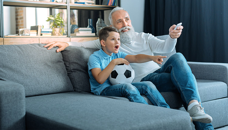 Großvater und Enkel sitzen auf der Couch und schauen Fußball