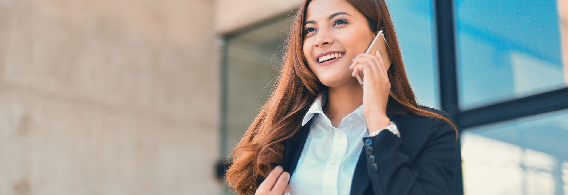 Frau telefoniert mit ihrem Smartphone vor einem Bürogebäude