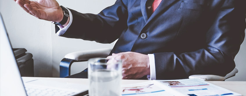 Mann sitzt hinter seinem Schreibtisch und erklärt etwas