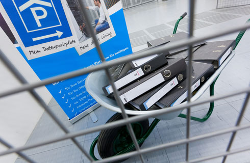 Schubkarre mit Aktenordnern hinter einem Gitter