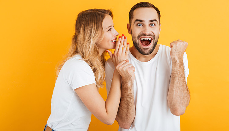 Frau flüstert einem Mann etwas ins Ohr