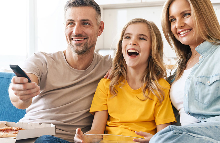 Schnellste Datenübertragung dank Glasfaserkabel - auch beim Streaming Familie sitzt auf der Couch und schaut zusammen Fernsehen