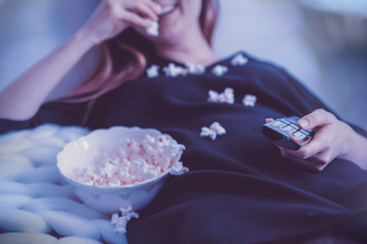 Frau liegt im Bett und isst Popcorn