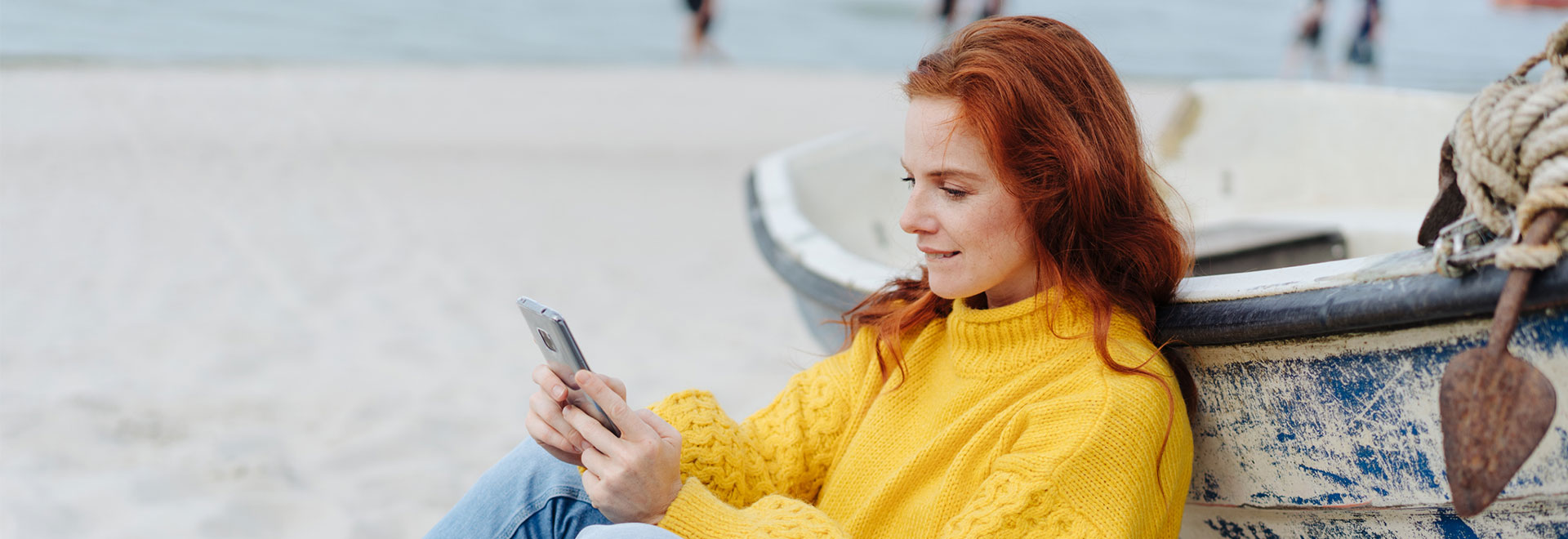 Frau sitzt mit ihrem Smartphone am Strand