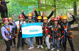 DOKOM21 Mitarbeiter mit Schülern und Lehrer mit Sicherheitsgurten und Helmen vor einem Hochseilgarten